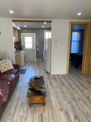 A modern living room with a wooden coffee table, a red leather sofa, and a kitchen area with wooden cabinets and a refrigerator. - Fabulous 2 Beds-1Bath  Back Terrace- Front Balcony @ Plateau Mont Royal (Montréal)