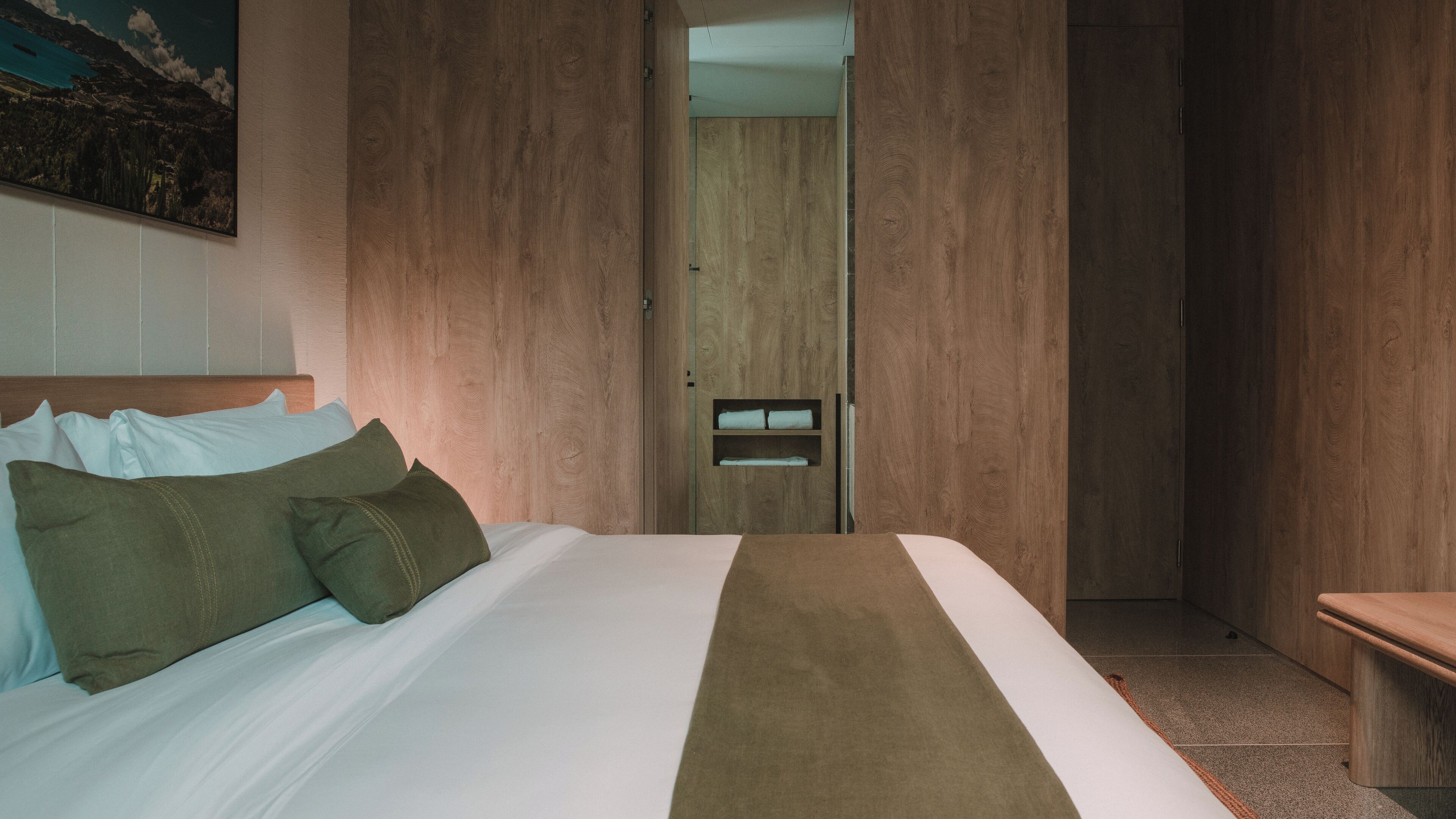 Una habitación de hotel con una cama, un armario de madera, un banco y un cuadro en la pared.