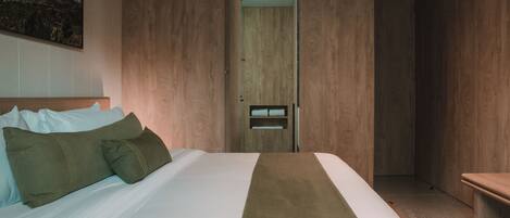Una habitación de hotel con una cama, un armario de madera, un banco y un cuadro en la pared.