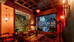 Una habitación acogedora con pared de ladrillo, sofá de cuero, mesa de centro de madera y vista a la ciudad iluminada de noche.
