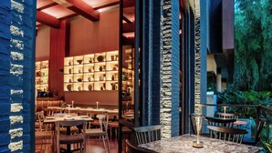 An indoor dining area with tables and chairs, a bar area with shelves, and a view of greenery outside.