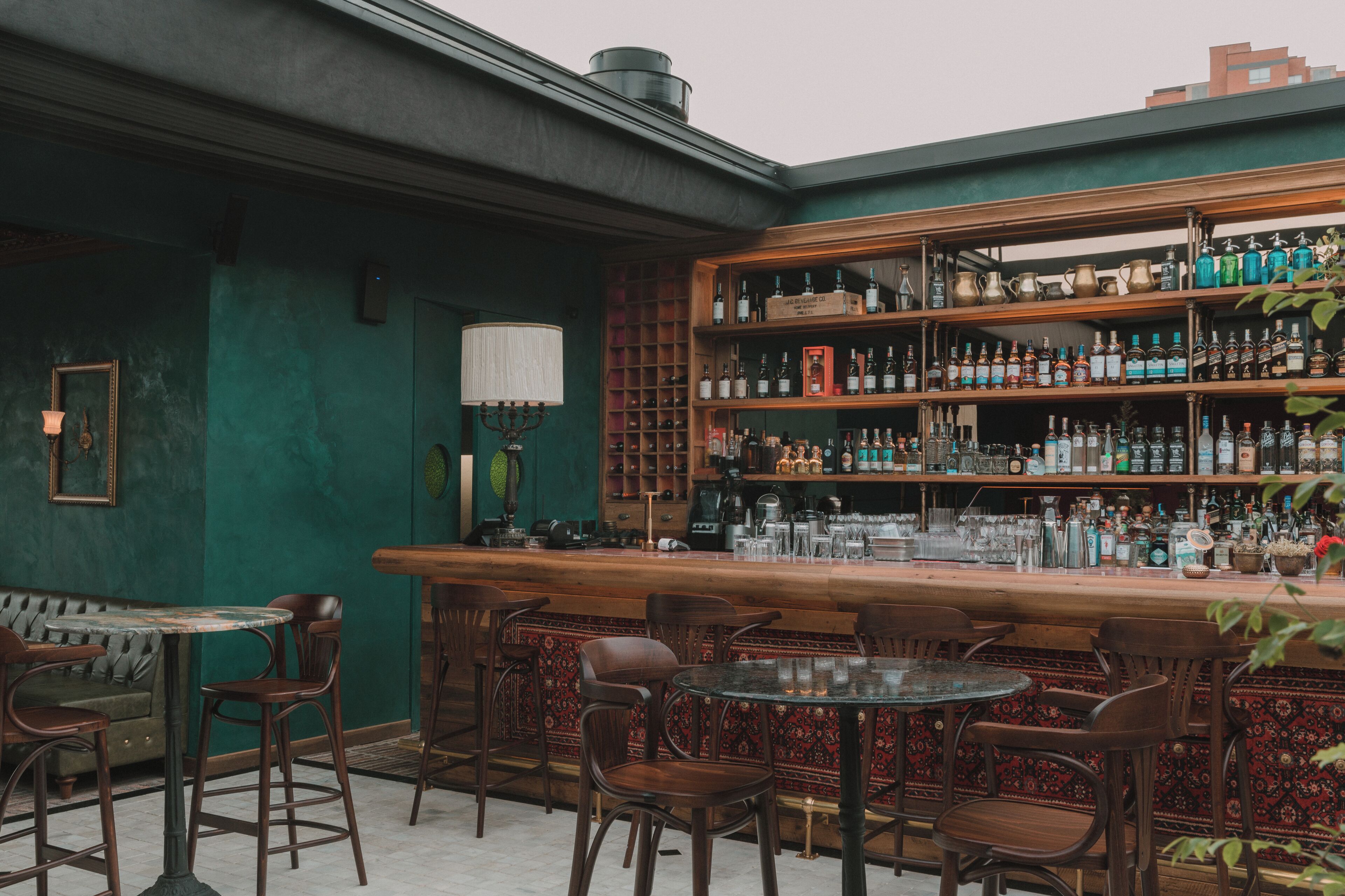 Una zona de bar con estantes de madera llenos de botellas, una barra y varias mesas y sillas de madera.