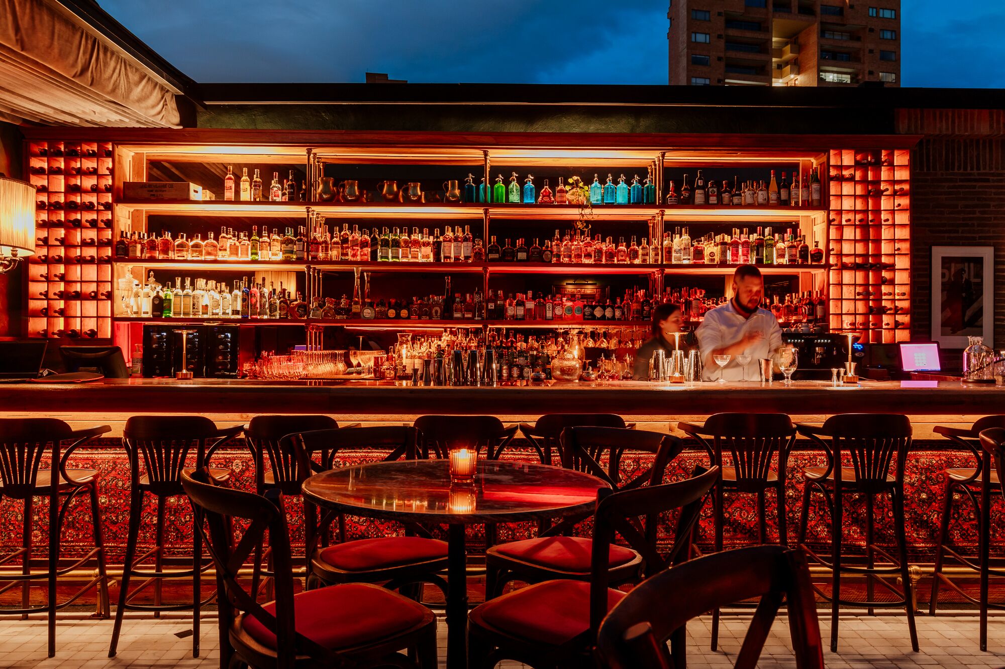 Eine Bar mit mehreren Flaschenregalen, einem Barkeeper und roten Sitzmöglichkeiten.