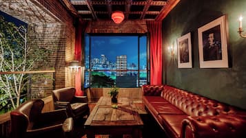 Un salón acogedor con un sofá de cuero, una mesa de centro de madera y sillones de cuero. Un ventanal ofrece vistas a un horizonte urbano nocturno.