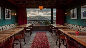 A restaurant with a view of mountains and a cityscape through large windows, featuring wooden tables and cushioned booths.