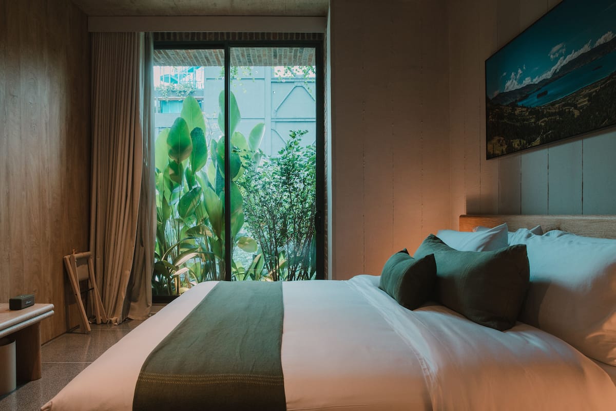 Habitación de hotel con una cama grande, vista a zonas verdes por una ventana y un cuadro en la pared.