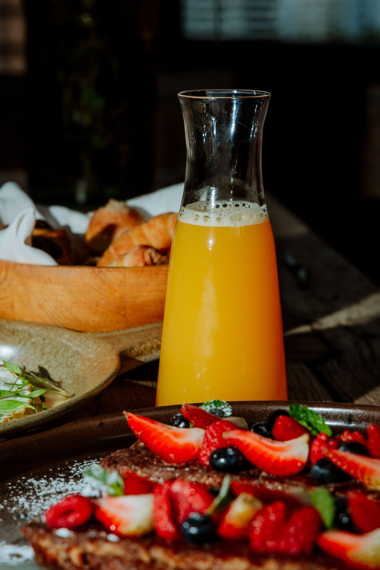 A breakfast setting with a glass of orange juice, a plate of strawberries, and a pastry.