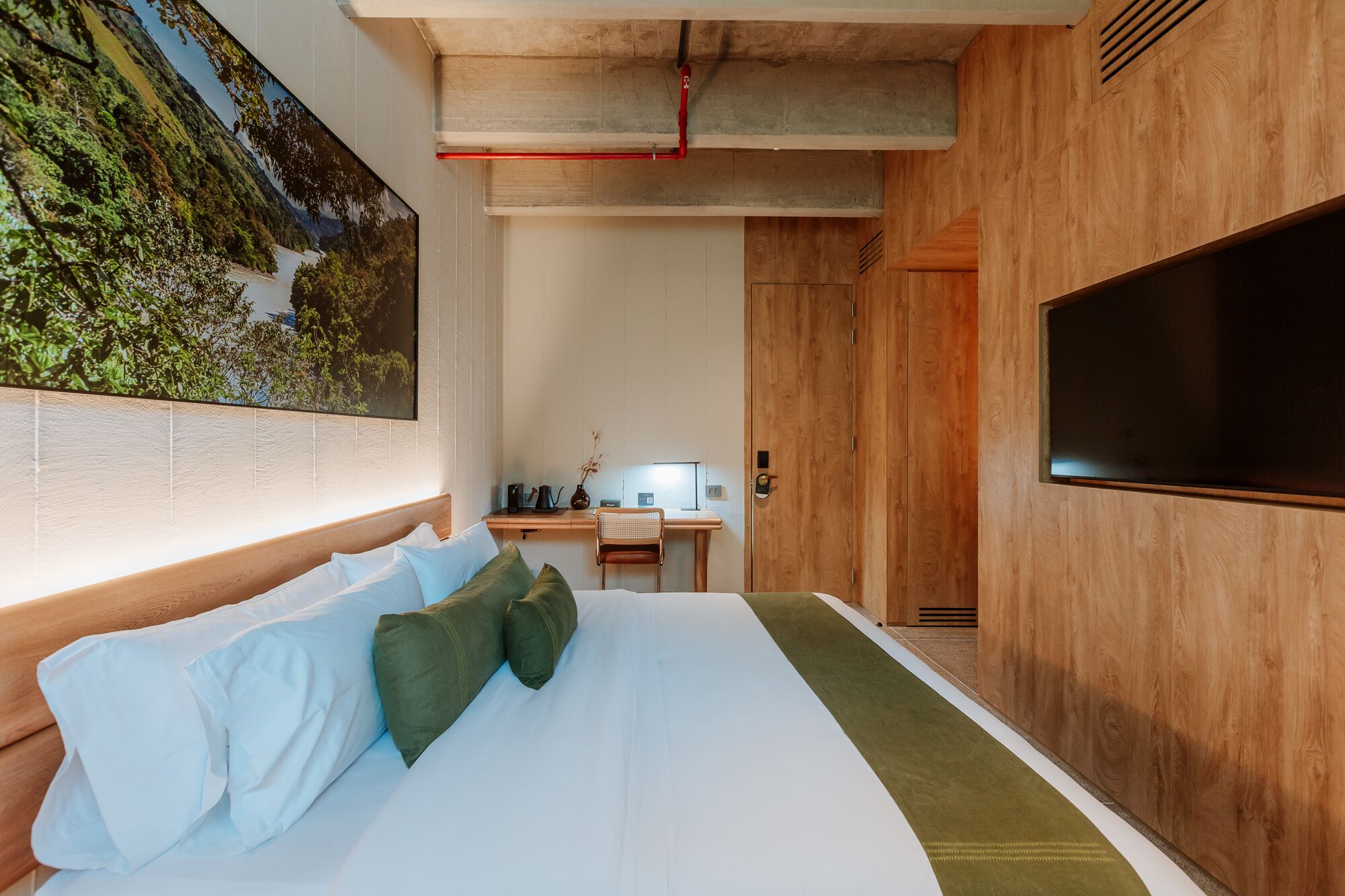 A hotel room with a large bed, a desk, a television, and a mural on the wall.