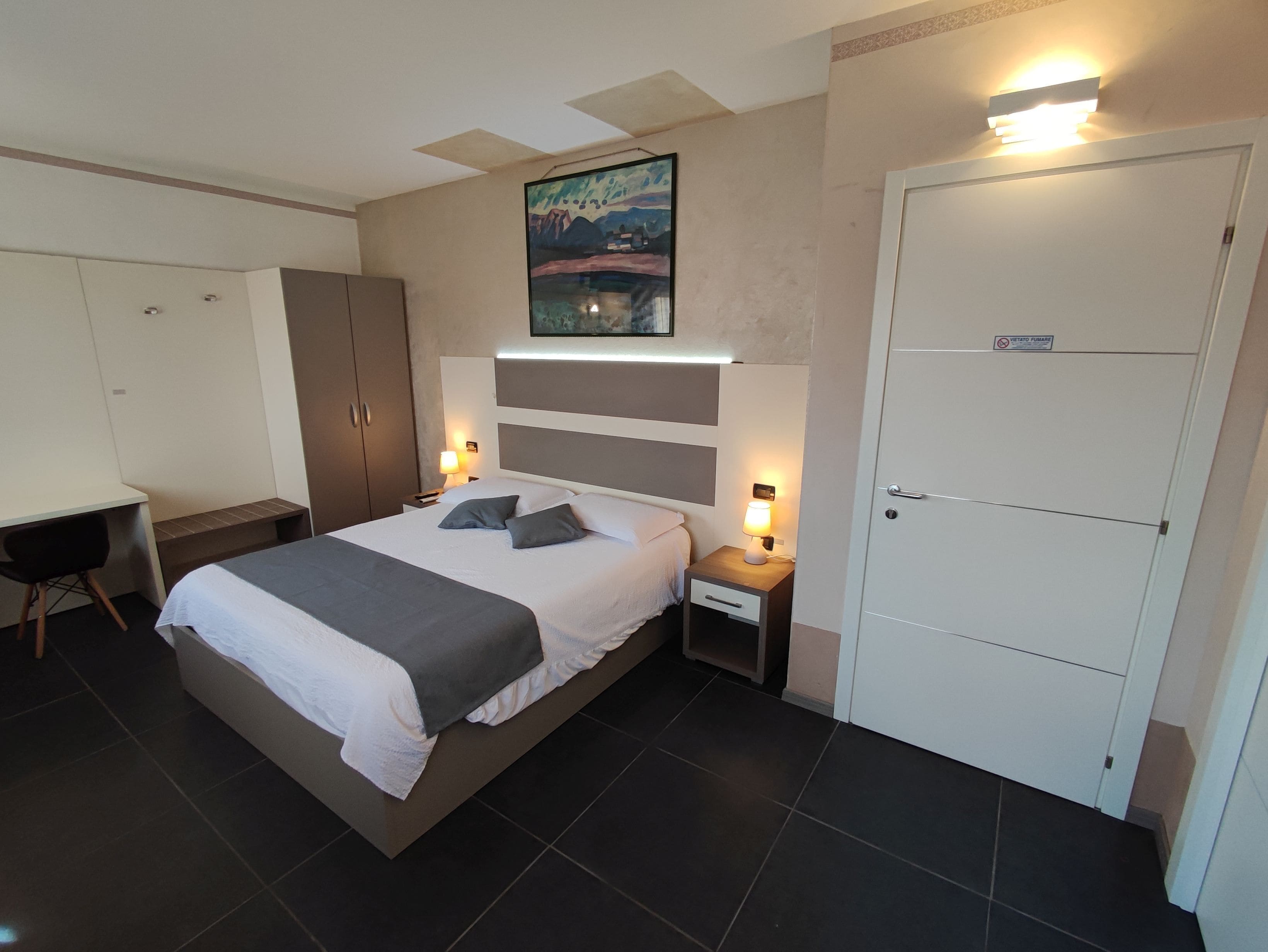 Una camera d'hotel moderna con un letto, comodini, una scrivania e un armadio.
