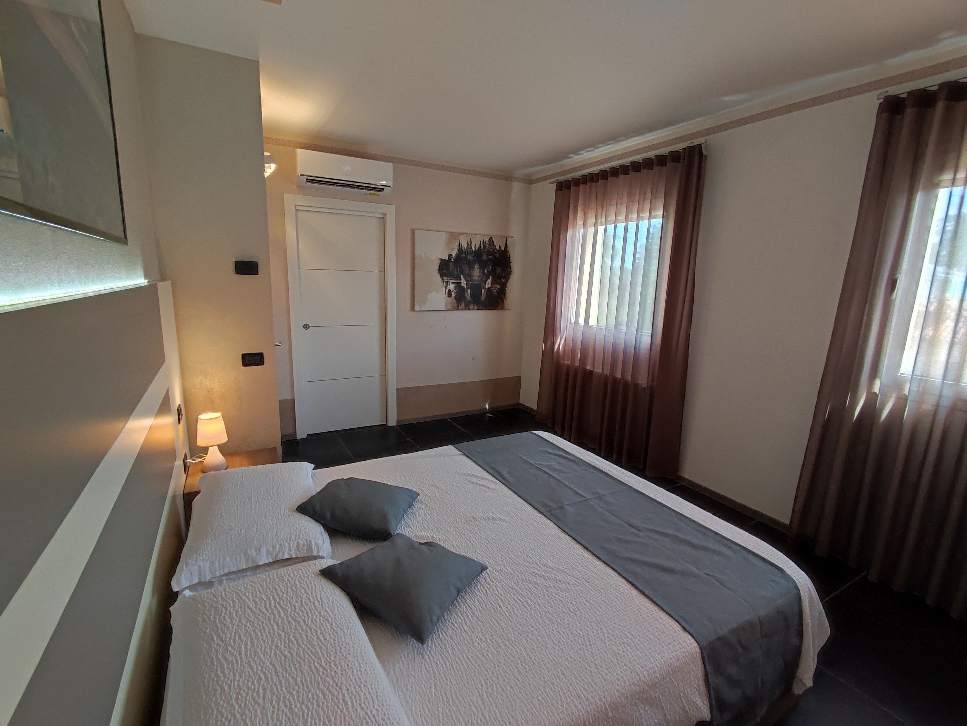 A hotel room with a large bed, a bedside lamp, a door, and a window with curtains.