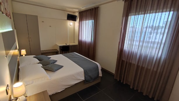 A hotel room with a bed, bedside lamp, desk, chair, and a TV mounted on the wall. - Therra Lodge (Preganziol)