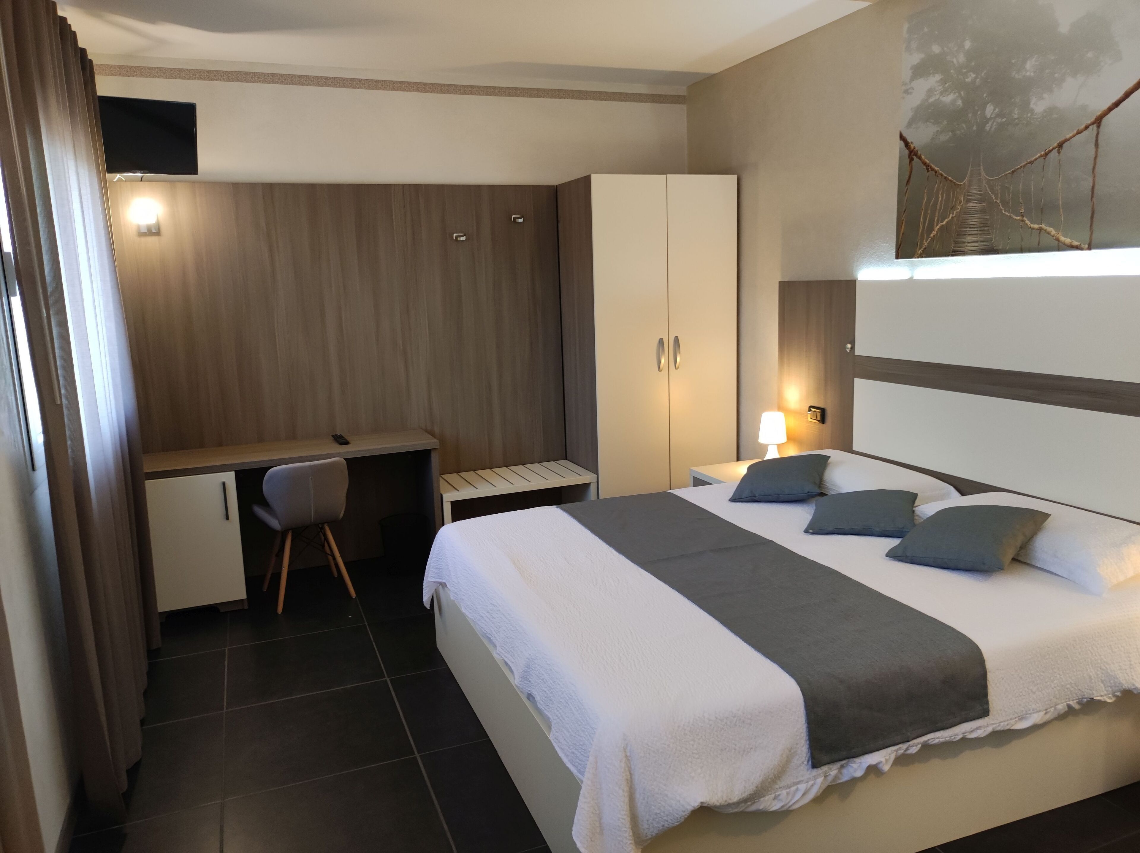 Una habitación de hotel con cama, escritorio, silla, armario y un cuadro en la pared.