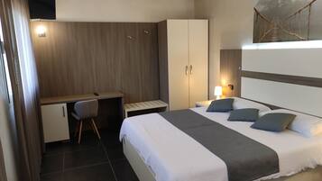 Una habitación de hotel con cama, escritorio, silla, armario y un cuadro en la pared.