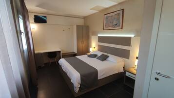 Een hotelkamer met een bed, nachtkastjes, een bureau, een stoel, een kledingkast en een televisie aan de muur.