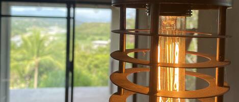 A hanging light fixture with a spiral design, a visible bulb, and a view of a balcony with greenery outside.