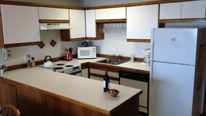 Una cucina con mobili in legno, un frigorifero bianco, un forno a microonde, un piano cottura e un lavandino.