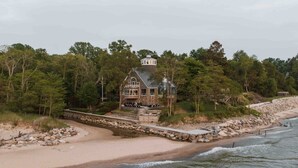 Ein Küstenhaus mit Steinaußenwand, einer Veranda und Blick auf Strand und Meer.