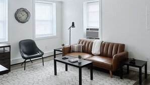 Un salon avec un canapé en cuir marron, un fauteuil noir, une table basse et une horloge murale.