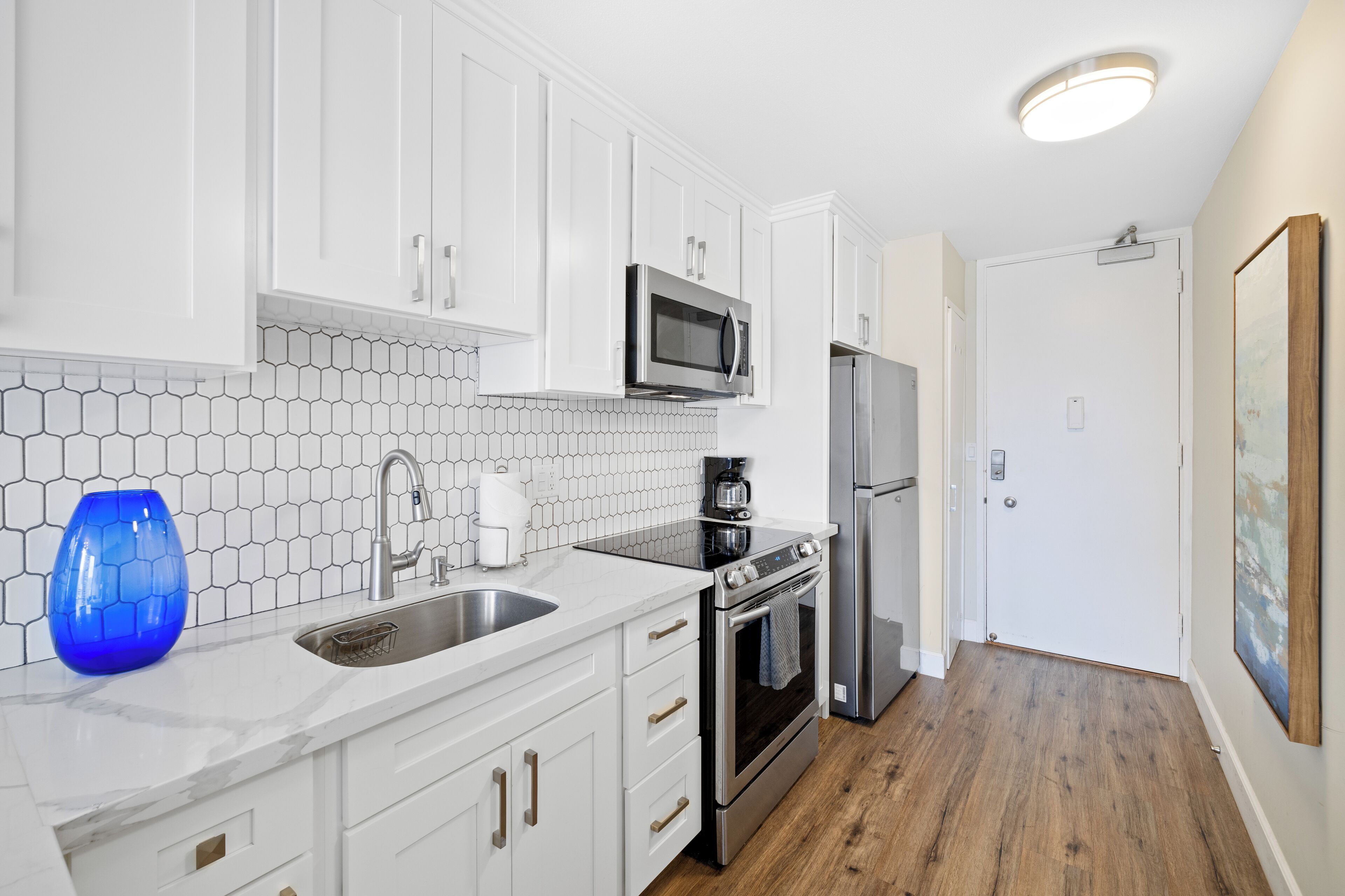 A modern kitchen with white cabinets, a stainless steel refrigerator, a microwave, and a stove.