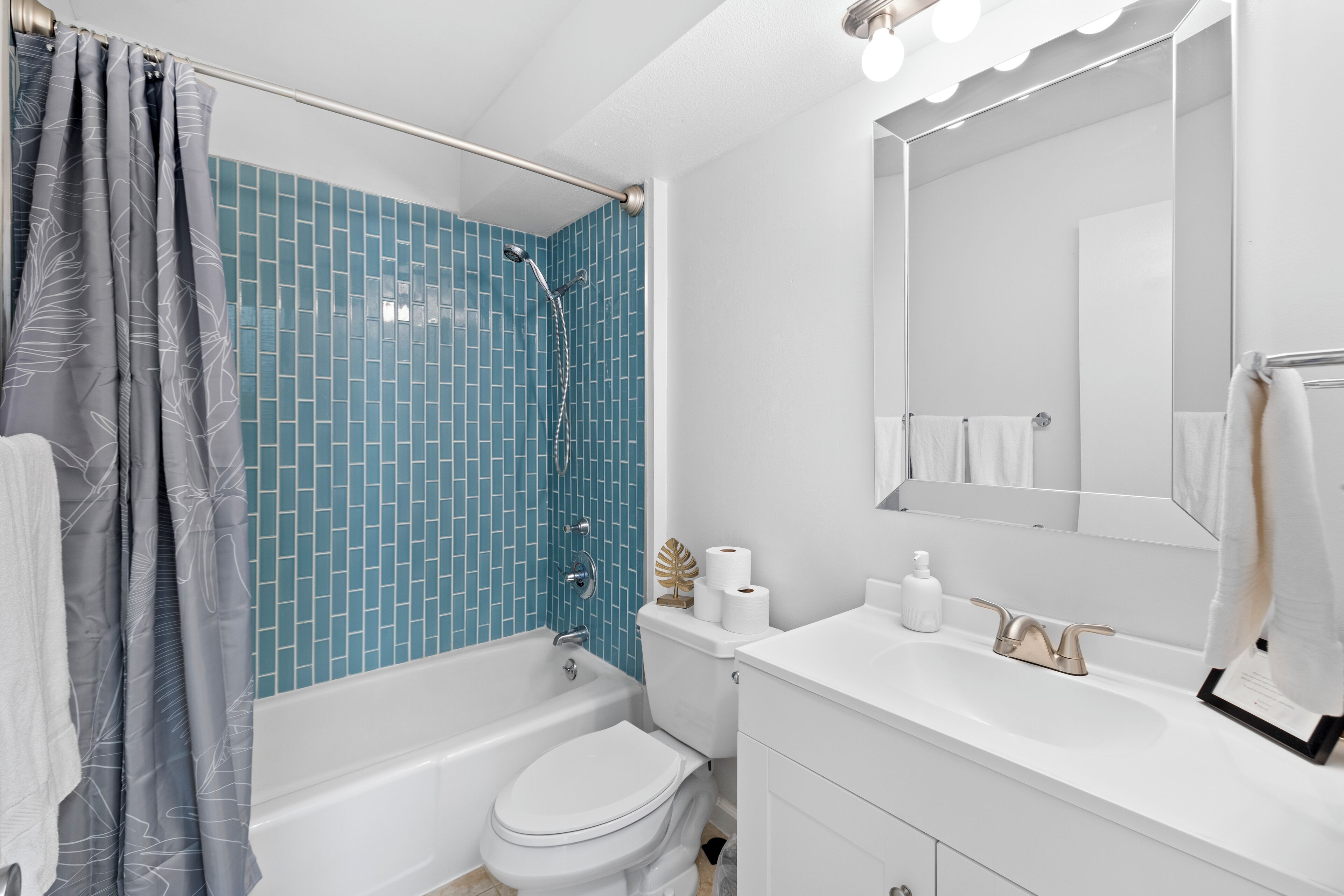 Ein modernes Badezimmer mit einer blauen Duschkabine, einer weißen Toilette und einem Waschtisch mit Spiegel.