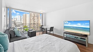 A modern hotel room with a large bed, a TV, a balcony with a view of the city, and a small dining area. - Ilikai Marina Vacations (Honolulu)