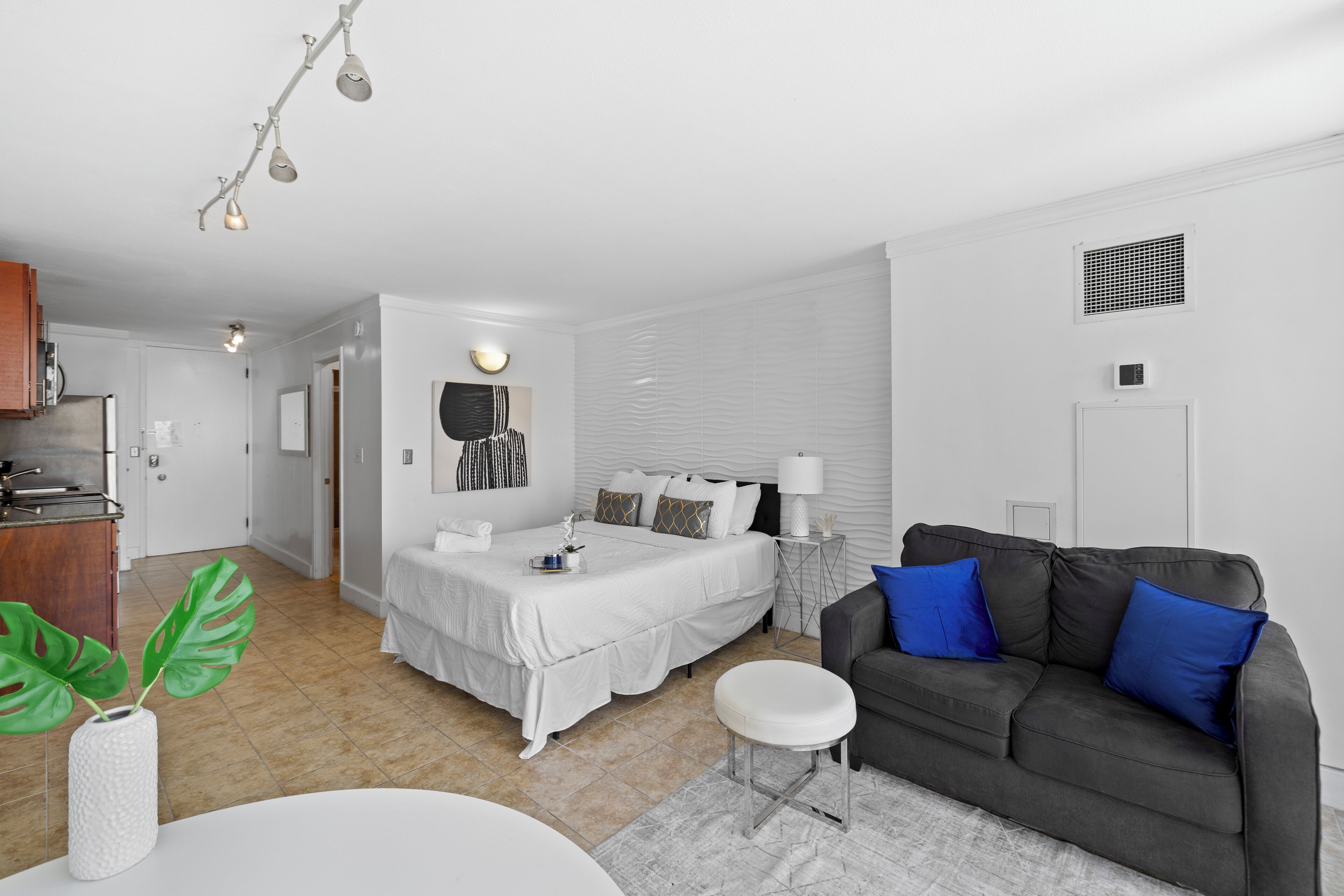 A modern bedroom with a bed, bedside table, and a grey sofa with blue cushions.