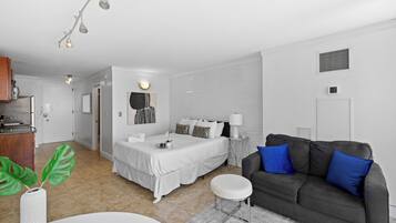 A modern bedroom with a bed, bedside table, and a grey sofa with blue cushions.
