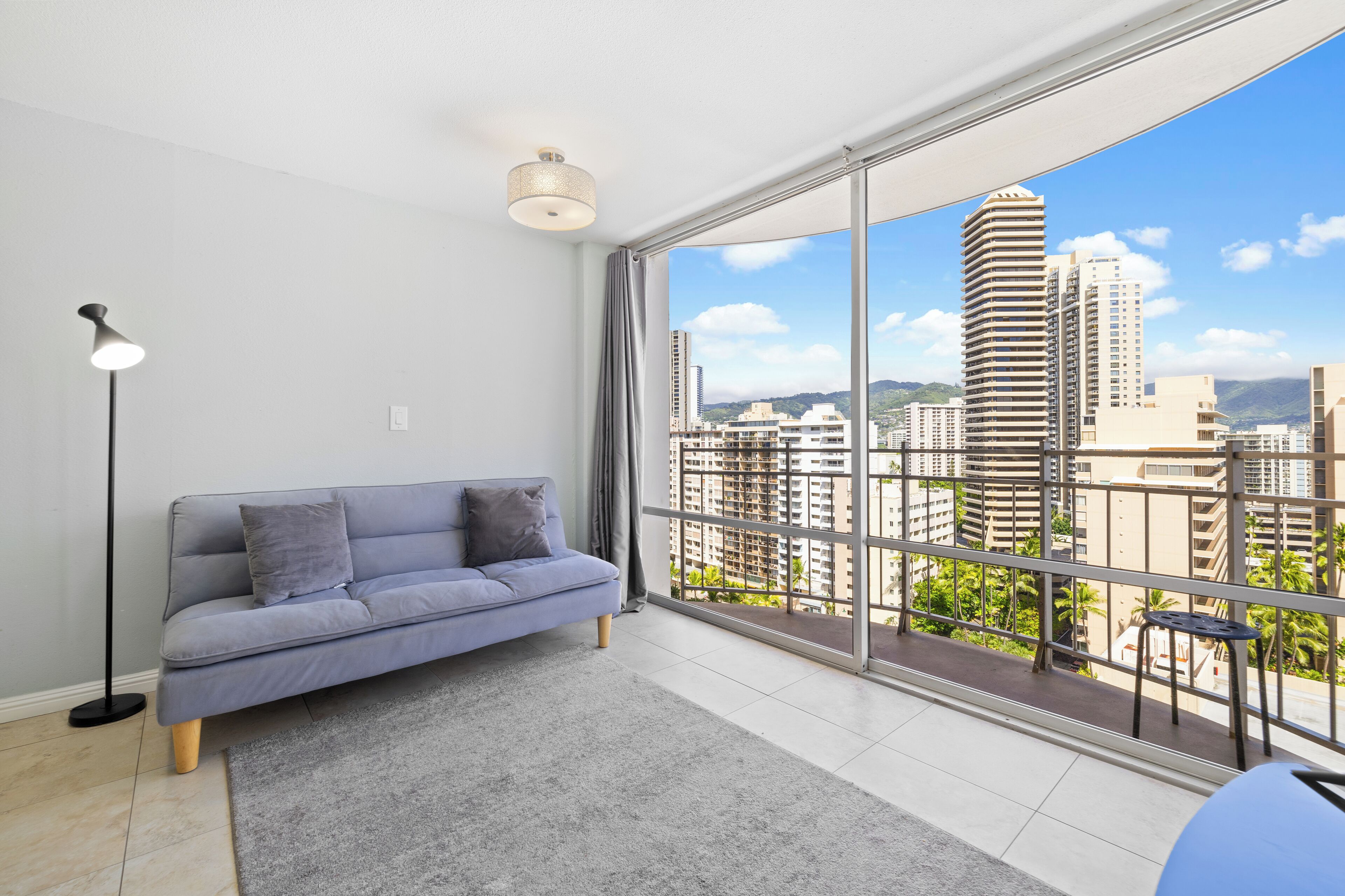Ein modernes Wohnzimmer mit einem grauen Sofa, einer Stehlampe und einem großen Fenster mit Blick auf die Stadt.