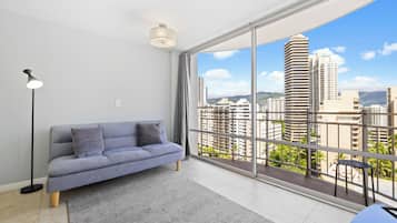A modern living room with a grey sofa, a floor lamp, and a large window offering a city view.