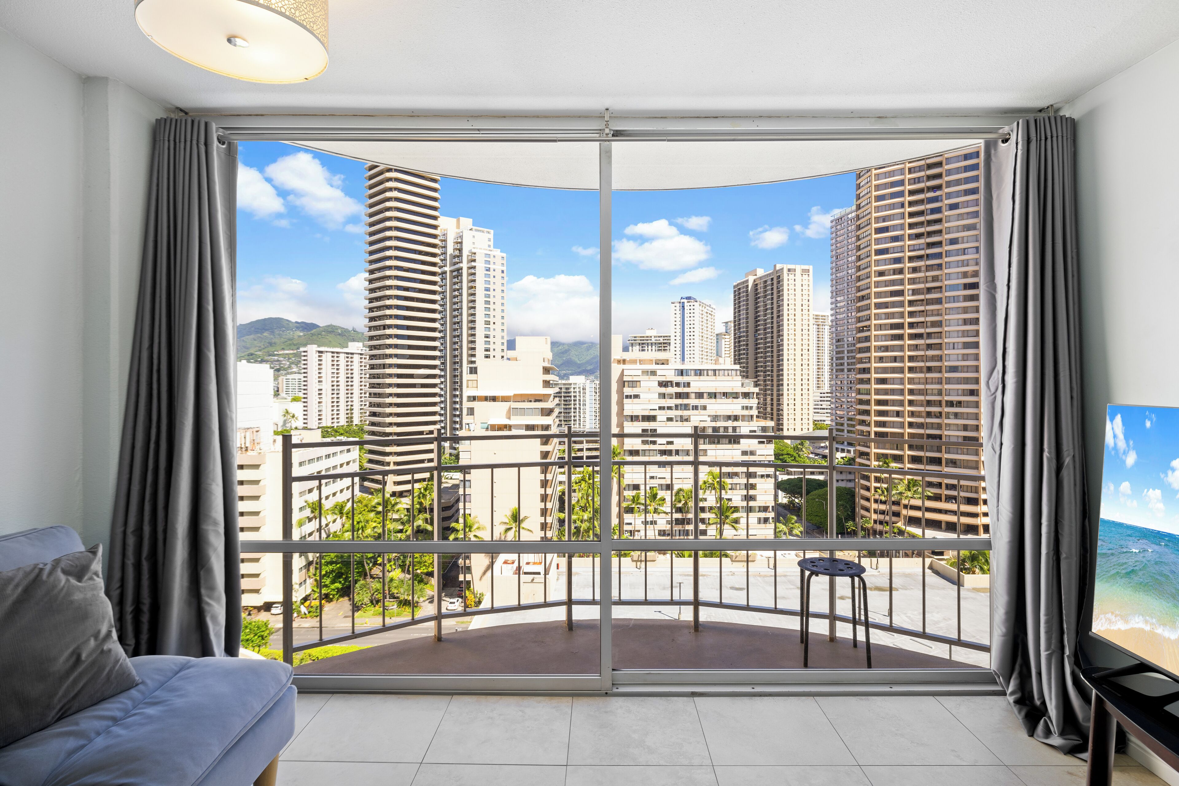 A modern hotel room with a large balcony, a sofa, and a TV.