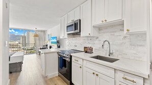 A modern kitchen with white cabinets, a stainless steel microwave, a sink, and a stove. - Ilikai Marina Vacations (Honolulu)