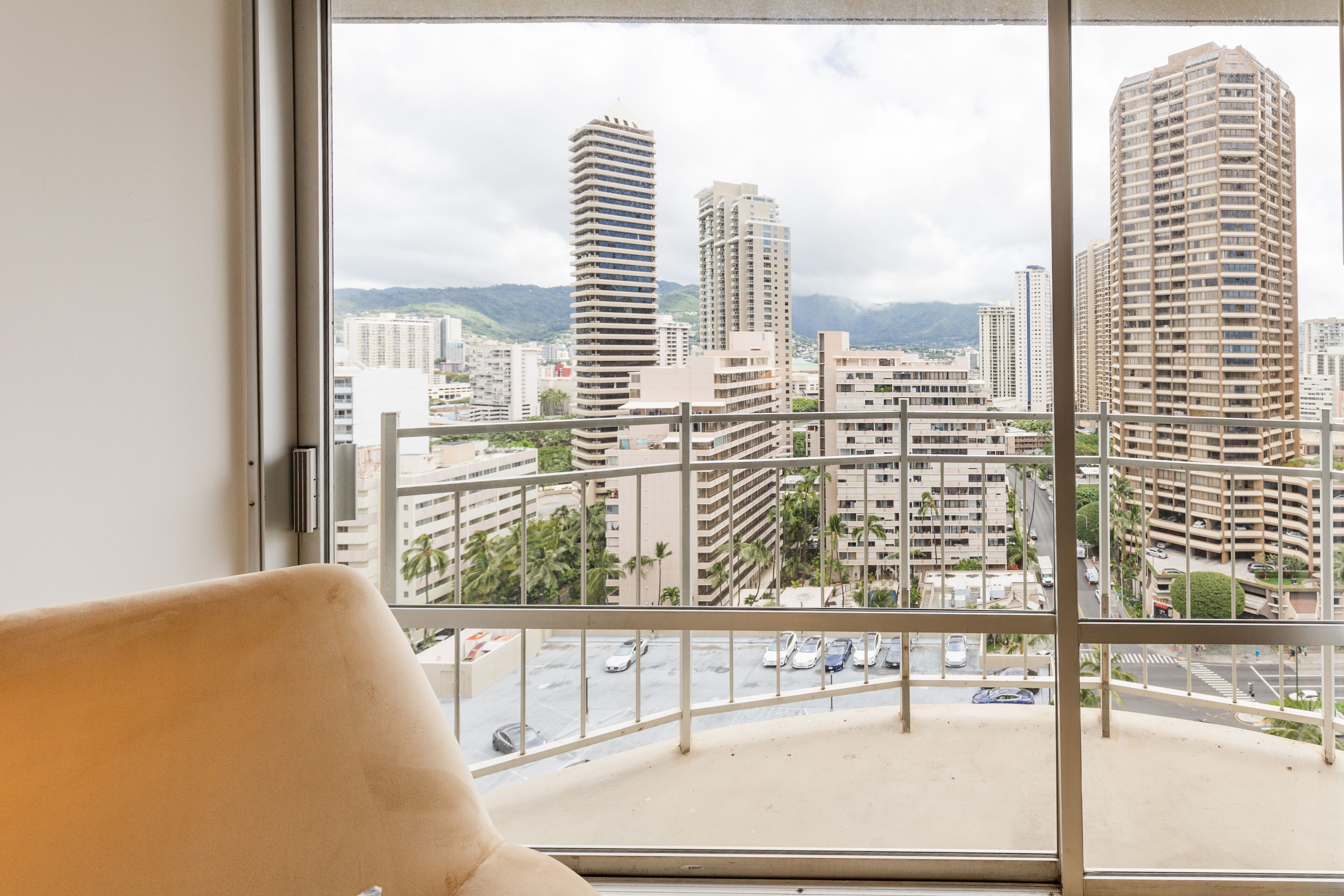 A view from a window of a building with multiple floors, a balcony, and a cityscape with tall buildings and a road with cars.