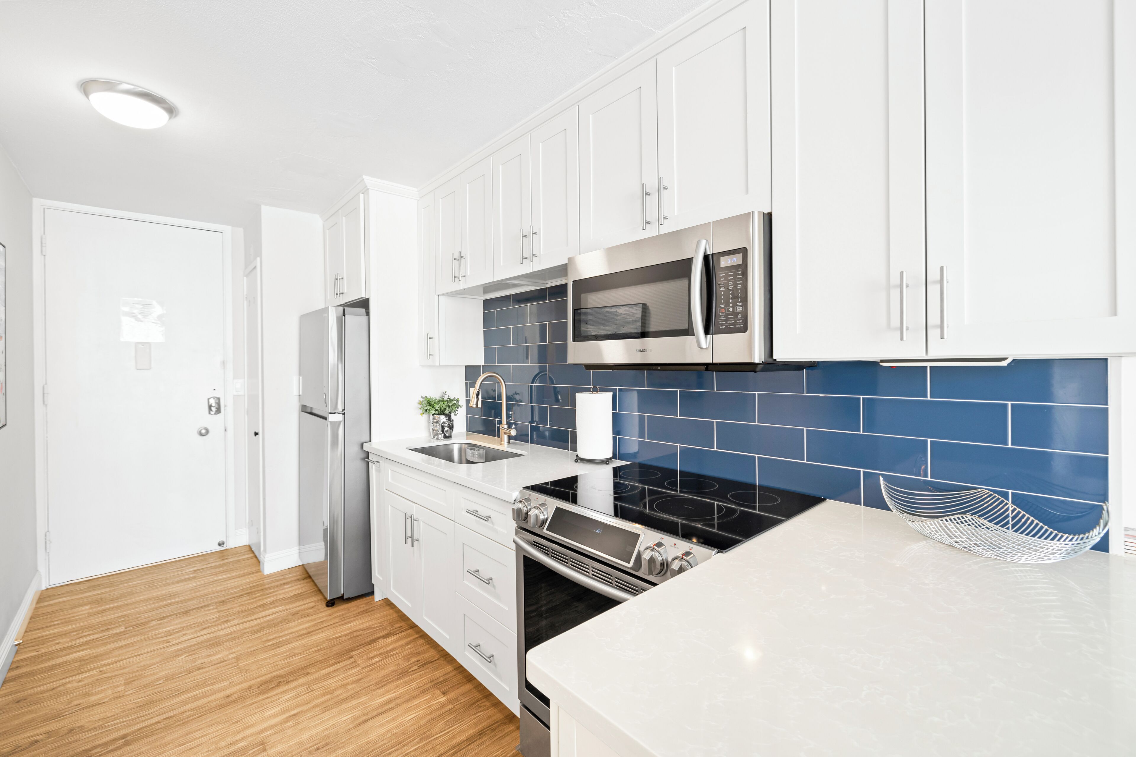 A modern kitchen with white cabinets, stainless steel appliances, and a blue tiled backsplash.