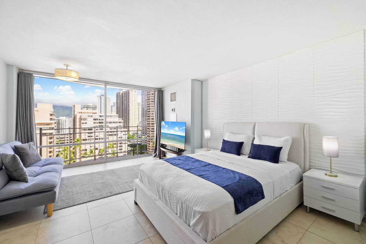 Quarto de hotel moderno com uma cama grande, um sofá, uma TV e uma varanda com vista para a cidade.