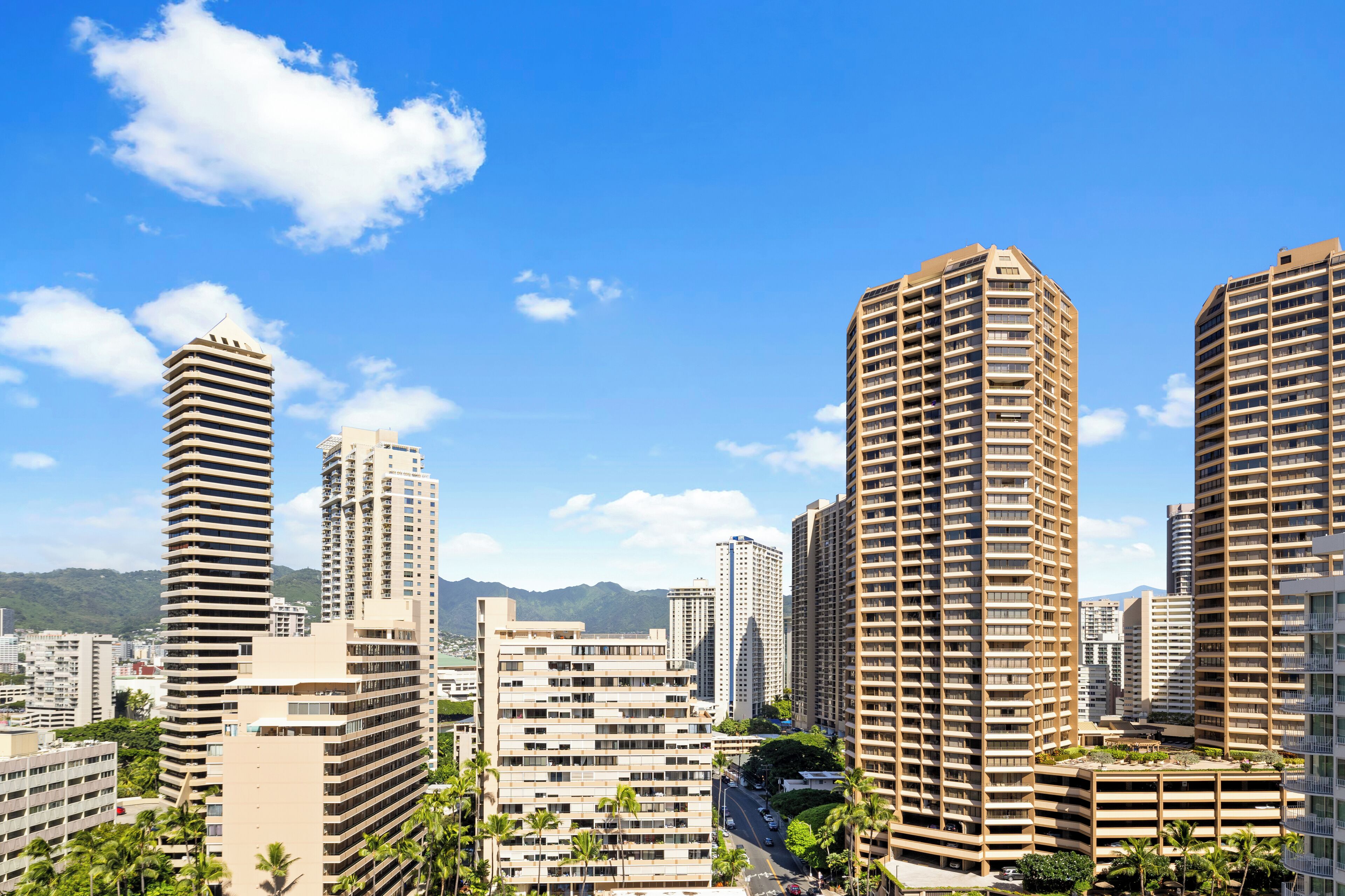 A cityscape with high-rise buildings, including a distinctive cylindrical structure and a tall rectangular building with a flat roof.