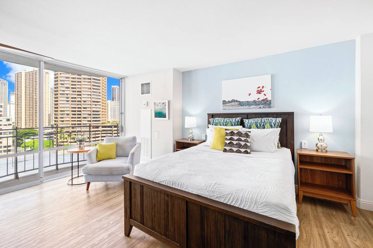 Quarto de hotel moderno com uma cama grande, um sofá, vista para edifícios altos e uma varanda.