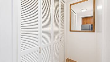 A hallway with white louvered closet doors and a mirror on the wall.
