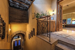 A grand staircase with a wrought iron railing, a stone archway, and a reception desk with potted plants.
