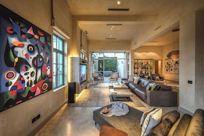 A spacious living area with a large abstract painting, comfortable seating, and a view to the outdoors.