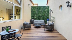 A patio with a sofa, chairs, and a table, a green wall, and a window. - The Pearl of Jaffa: 3BR Luxury with Patio (Tel Aviv-Yafo)