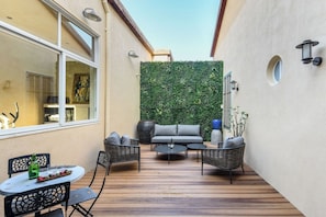 A patio with a sofa, chairs, and a table, a green wall, and a window.
