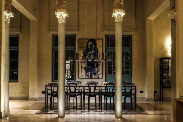 A lobby with a large painting, columns, and tables.