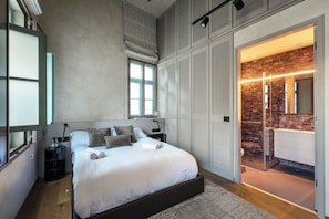 A bedroom with a large bed, a wardrobe, a bathroom with a shower, and a view of the outside.
