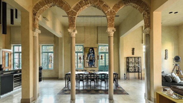 A spacious interior with a central dining area, stone arches, and a view through large windows. - The Pearl of Jaffa: 3BR Luxury with Patio (Tel Aviv-Yafo)