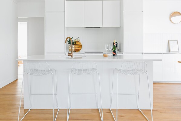 Una cocina moderna con armarios blancos, una isla central con taburetes y un cuenco de madera decorativo.