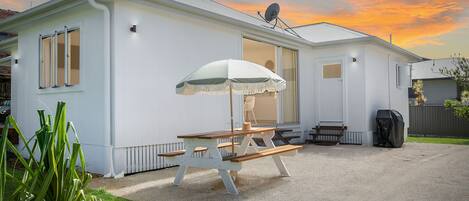A white mobile home with a picnic table and umbrella, a satellite dish, and a covered grill area.