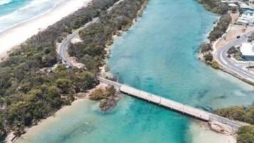 An aerial view of a coastal area with a long bridge connecting two land masses, clear turquoise waters, and a sandy beach.