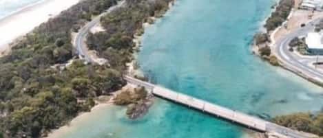 An aerial view of a coastal area with a long bridge connecting two land masses, clear turquoise waters, and a sandy beach.