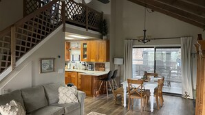 A spacious living area with a staircase, a dining table with chairs, a kitchen with wooden cabinets, and a large sliding glass door leading to an outdoor patio. - Mountain Pine Main House on Quiet Cul-de-sac-3 Decks-Views of Forest + Hot Tub! (Flagstaff)