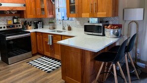 A kitchen with wooden cabinets, a microwave, a stove, and a checkered rug. - Mountain Pine Main House on Quiet Cul-de-sac-3 Decks-Views of Forest + Hot Tub! (Flagstaff)